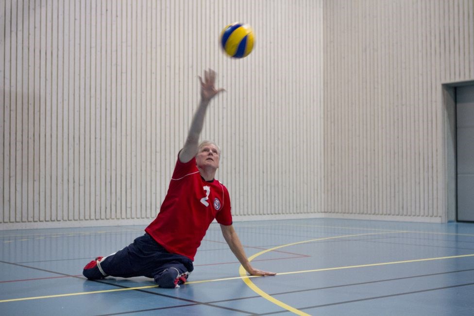 Mann spiller volleyball på gulvet i en hall. Foto