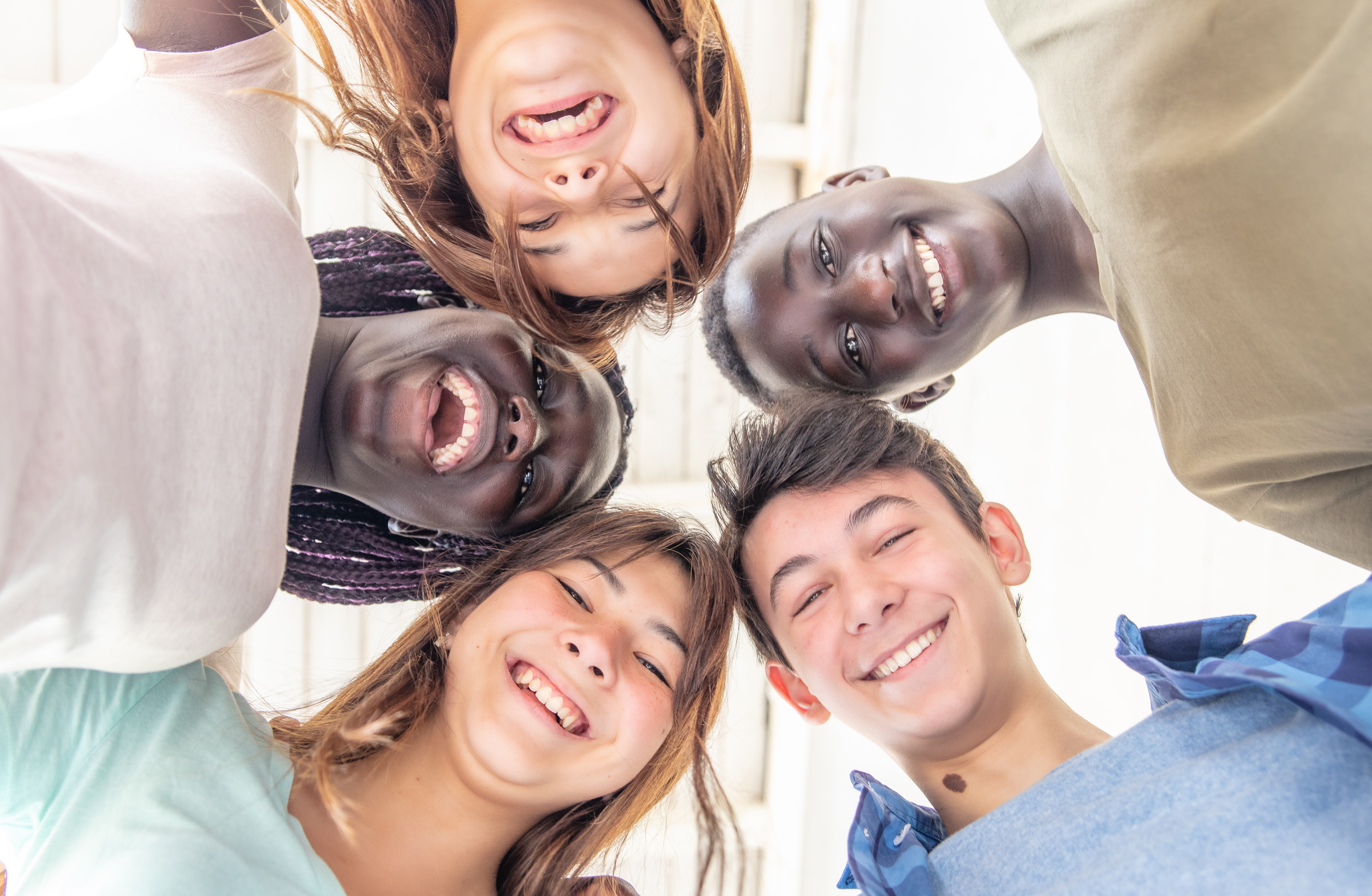 Fem ungdommer som står i ring, smiler og titter ned på kamera. Ungdommene har ulik hudfarge og bildet gir en følelse av fellesskap.  