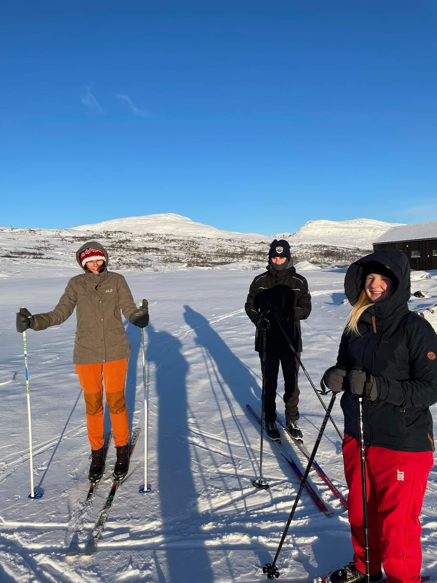 Foto av tre personer som går på ski i fjellet.
