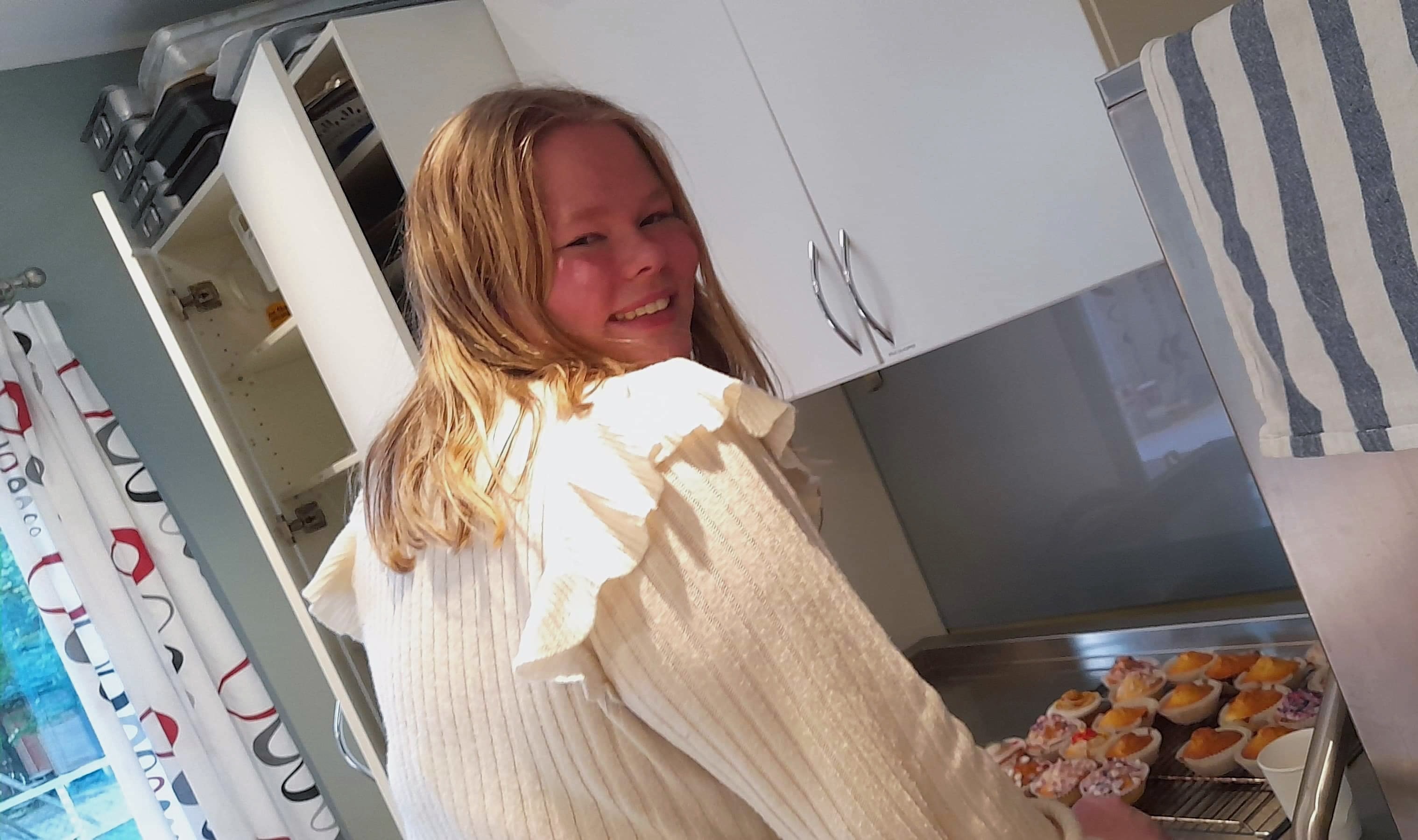 Foto av Kristine på kjøkkenet. Hun holder et brett med muffins. 