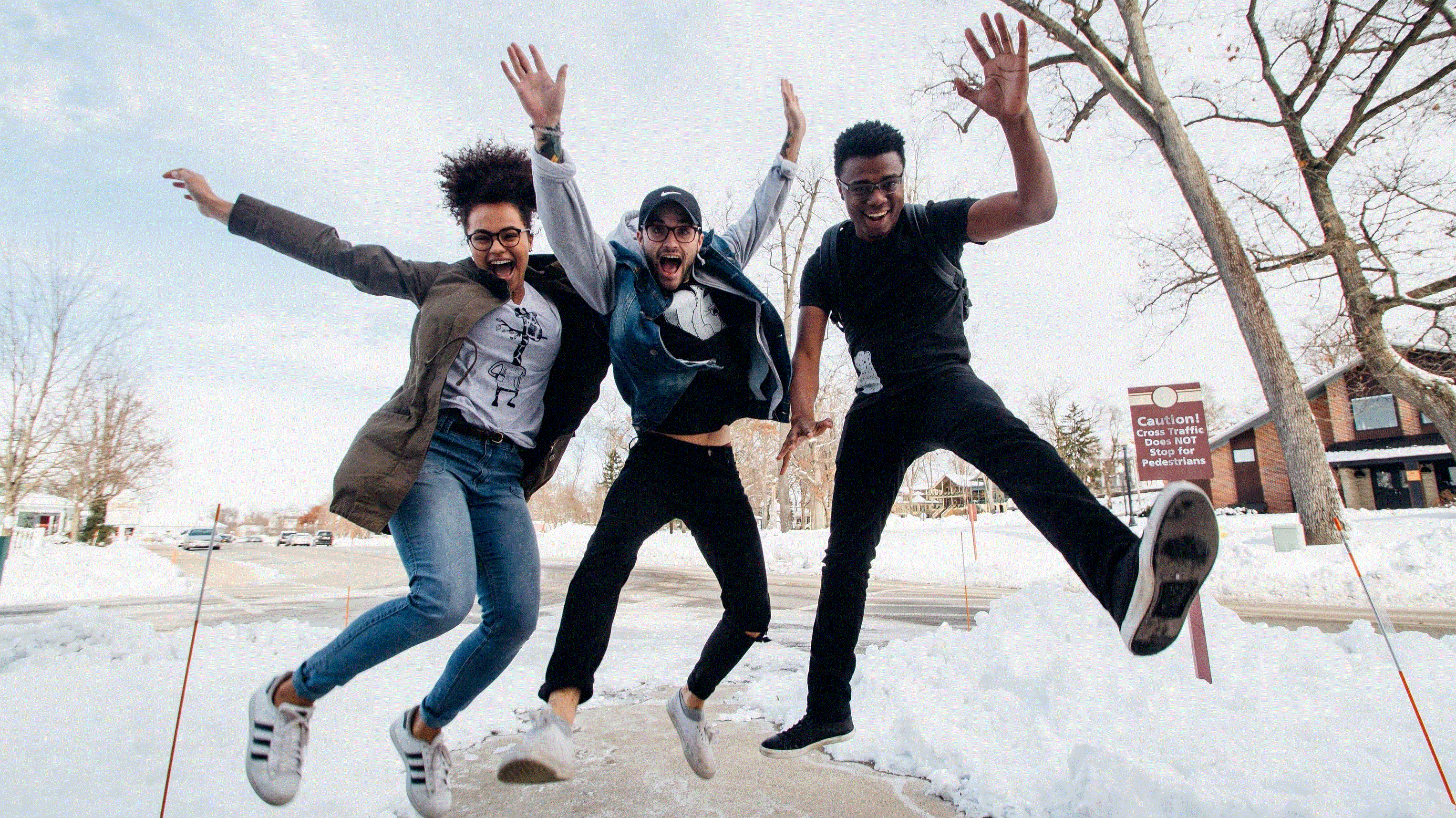 Tre unge mennesker som hopper ute. Det er snø.